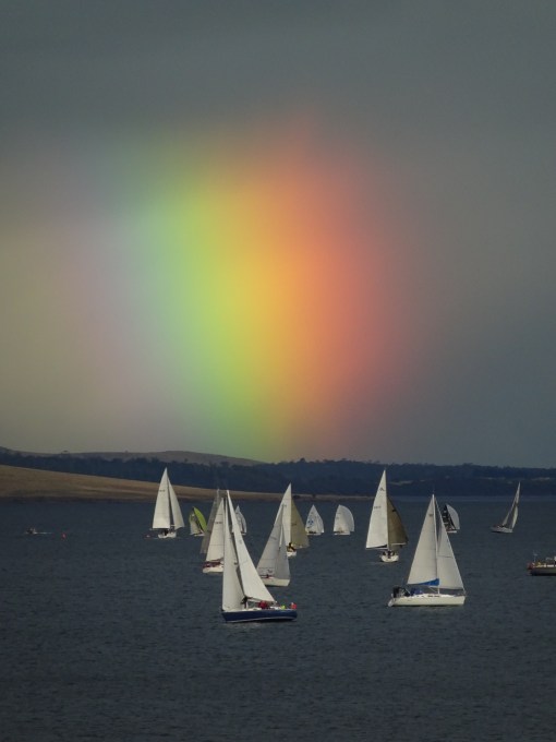 The yachts dance in the wind as the diffuse rainbow behind them lights up the sky.